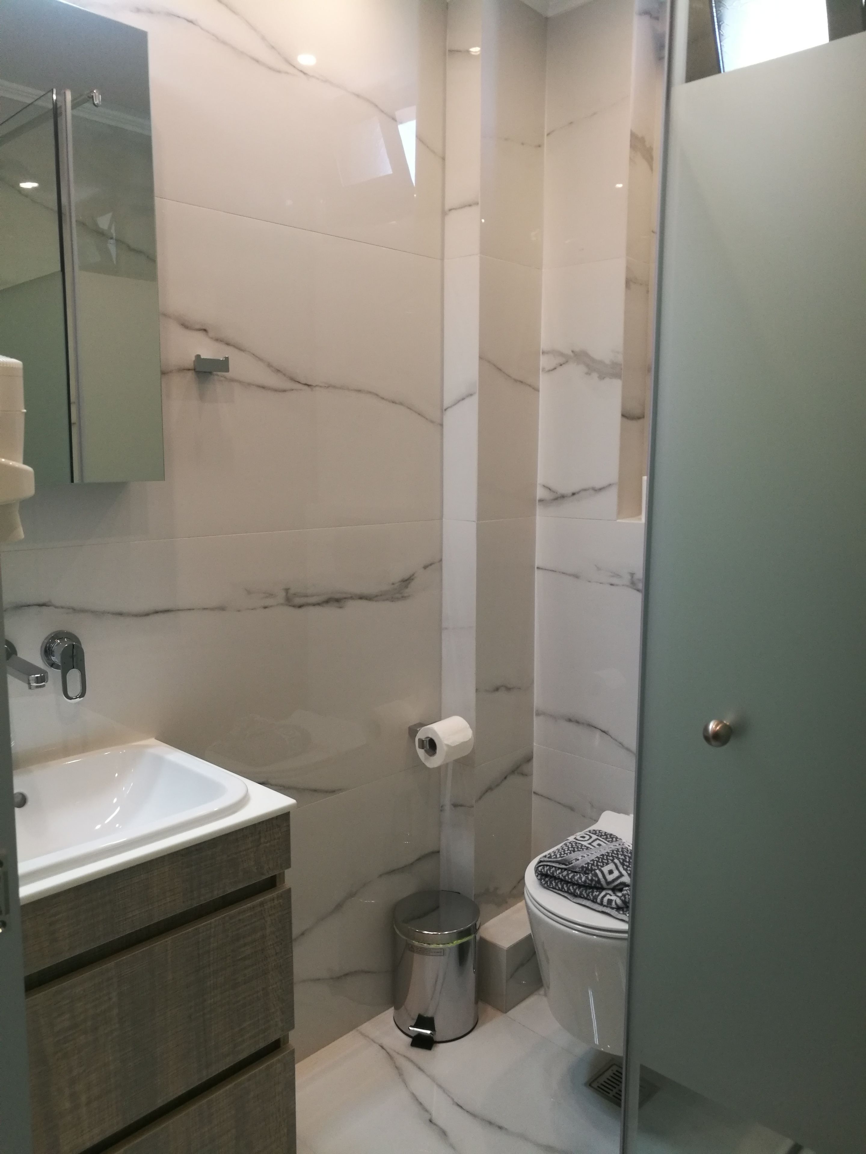 Een badkamer met een marmeren wand, een wastafel, een toilet en een prullenbak.