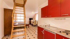 Une cuisine avec des meubles de rangement rouges, une échelle en bois et un sol carrelé.
