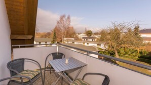 Un balcon avec des fauteuils et une table en osier, donnant sur un jardin et des immeubles.