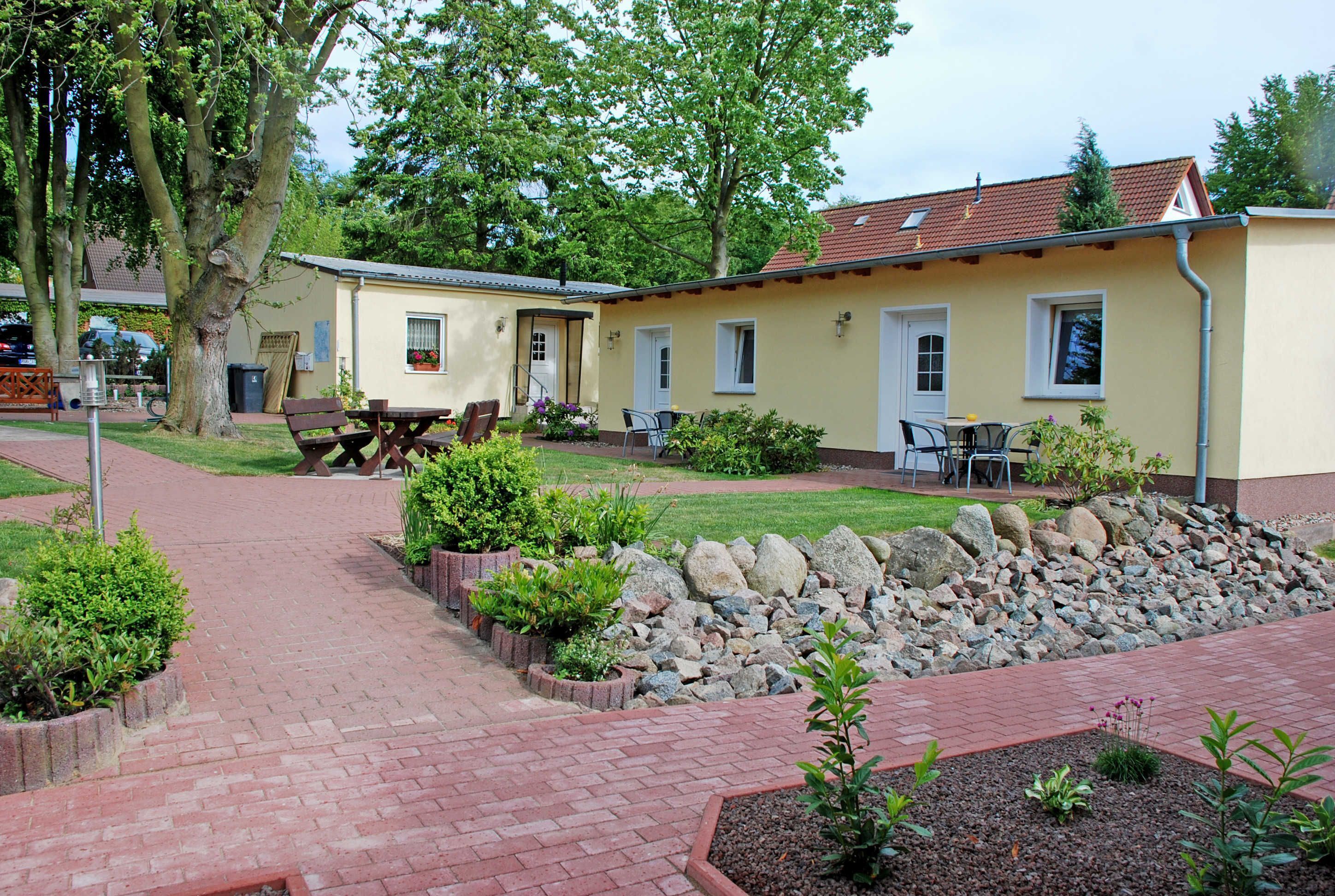 Ein Innenhof mit gepflastertem Weg, Sitzgelegenheiten im Freien und einer kleinen Gartenanlage mit Steinen und Pflanzen.