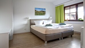 A bedroom with a bed, a window with curtains, a radiator, and a painting on the wall.