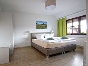 A bedroom with a bed, a window with curtains, a radiator, and a painting on the wall.