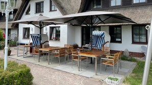Ein Gebäude mit einem Strohdach und einer Terrasse mit Holztischen und -stühlen.