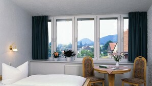 Hotellihuone, jossa on sänky, kaksi tuolia, pieni pöytä ja ikkuna, jossa on verhot.