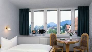 Ein Hotelzimmer mit einem Bett, zwei Stühlen, einem kleinen Tisch und einem Fenster mit Vorhängen.