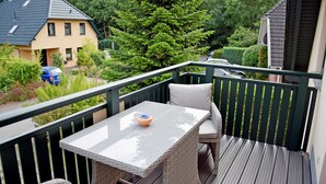 Un balcón con mobiliario de mimbre, una mesa y vistas a una casa y árboles.