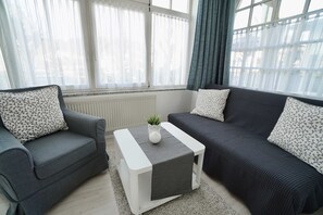 Un salon moderne avec deux canapés, une table basse et une vue sur l’extérieur grâce à de grandes fenêtres.