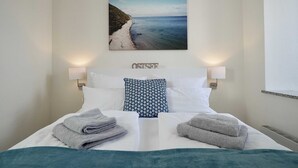 A neatly made bed with two pillows, a framed picture of a beach, and two bedside lamps. - 05 Ferienappartement Jasmund (H) - Apartment house Haus Arkona (Sellin)