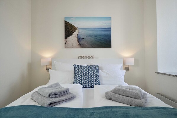 A neatly made bed with two pillows, a framed picture of a beach, and two bedside lamps.