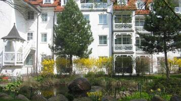 Un immeuble à plusieurs étages doté de balcons, un jardin avec des rochers et des plantes, et un étang.