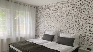 Ein modernes Schlafzimmer mit einem schwarzen Bett, weißer Bettwäsche und einem blumigen Wandpapier-Muster.