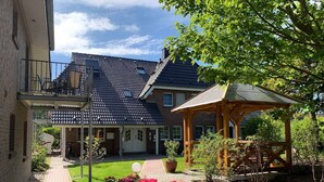 Ein Wohngebäude mit überdachter Terrasse, einem hölzernen Pavillon und einem Garten mit leuchtenden Blumen.