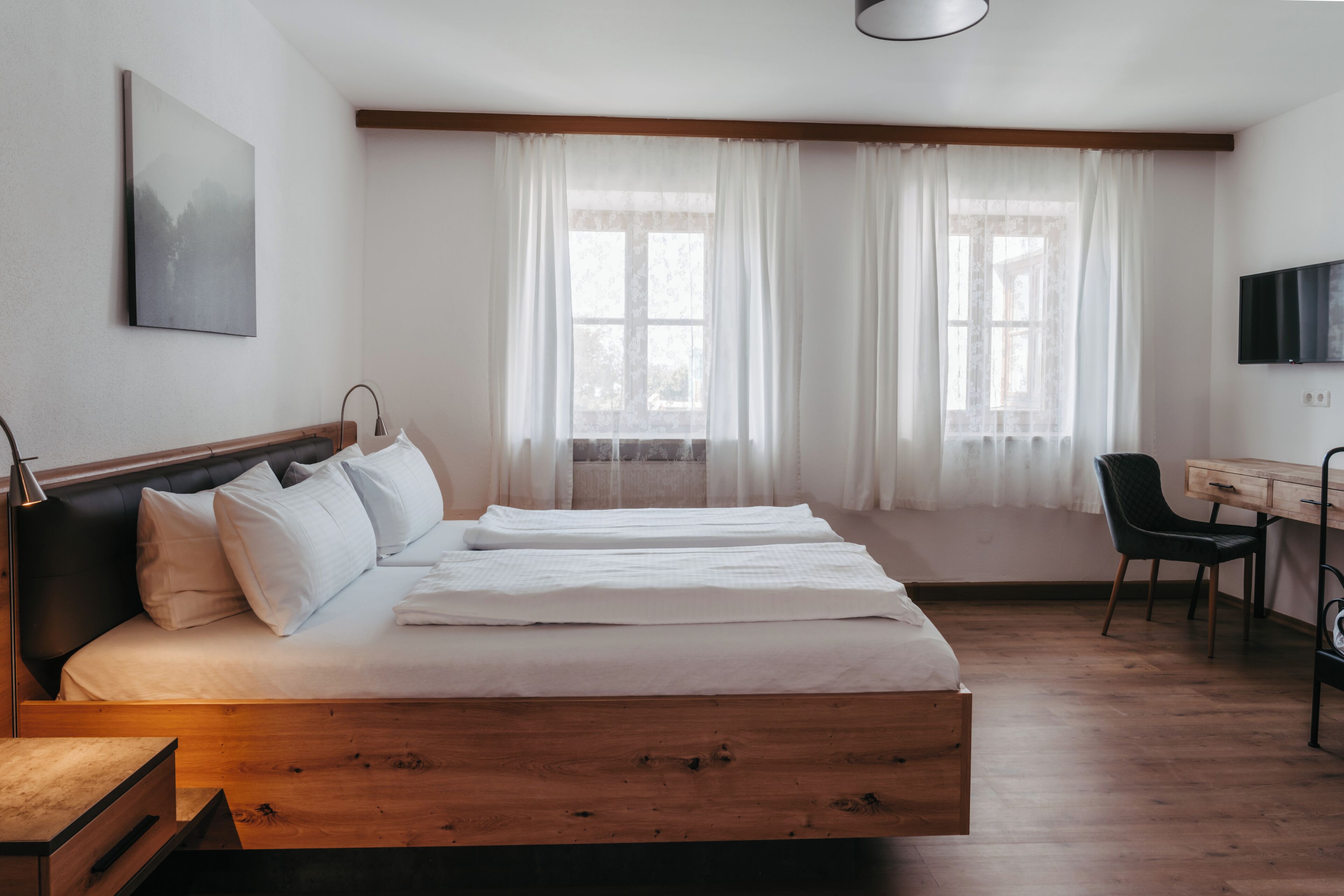 A bedroom with a wooden bed, a desk, a chair, and a TV on the wall.