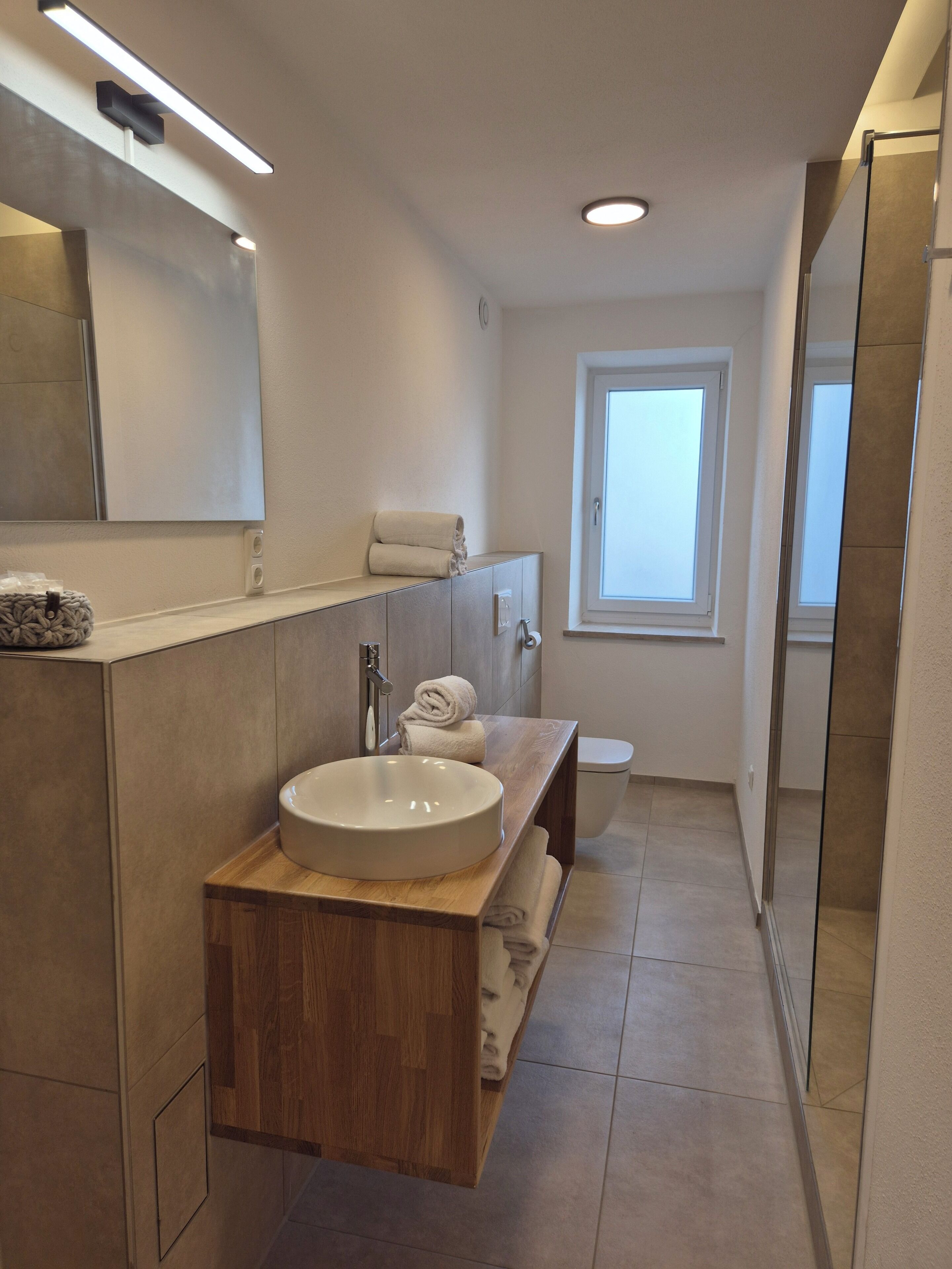 Un baño moderno con tocador de madera, un lavabo redondo, un espejo y una ventana.