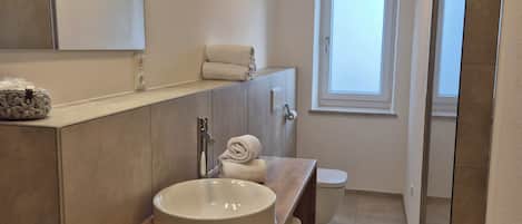 Un baño moderno con tocador de madera, un lavabo redondo, un espejo y una ventana.