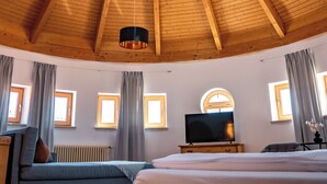 Techo circular de madera con tragaluz, una cama, un televisor y una ventana con cortinas.