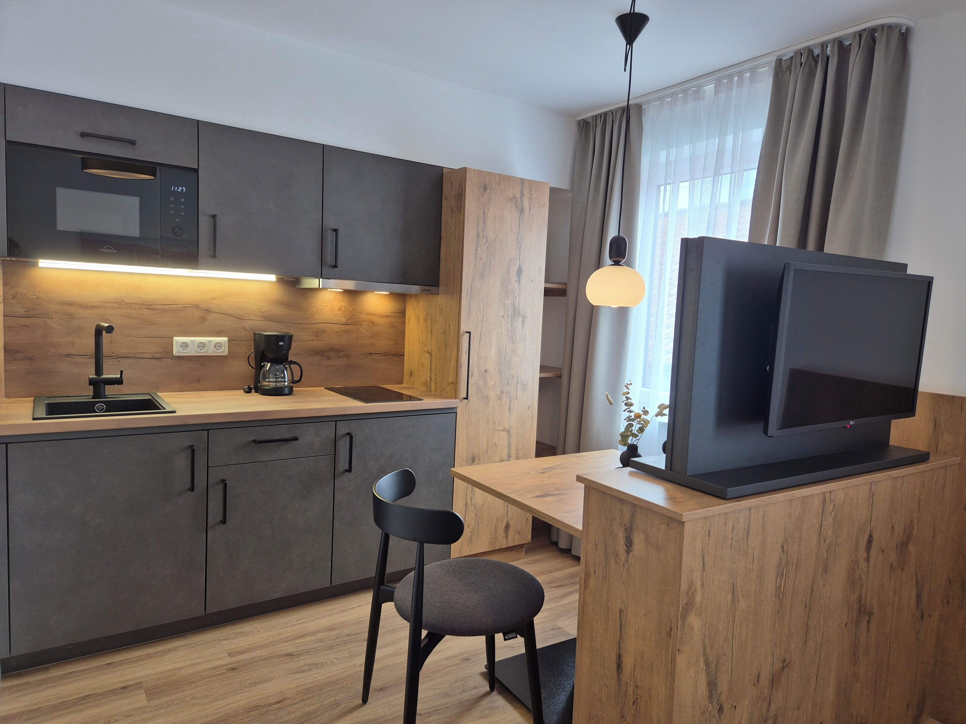 A modern kitchen with a built-in microwave, coffee maker, and a TV on a wooden stand.