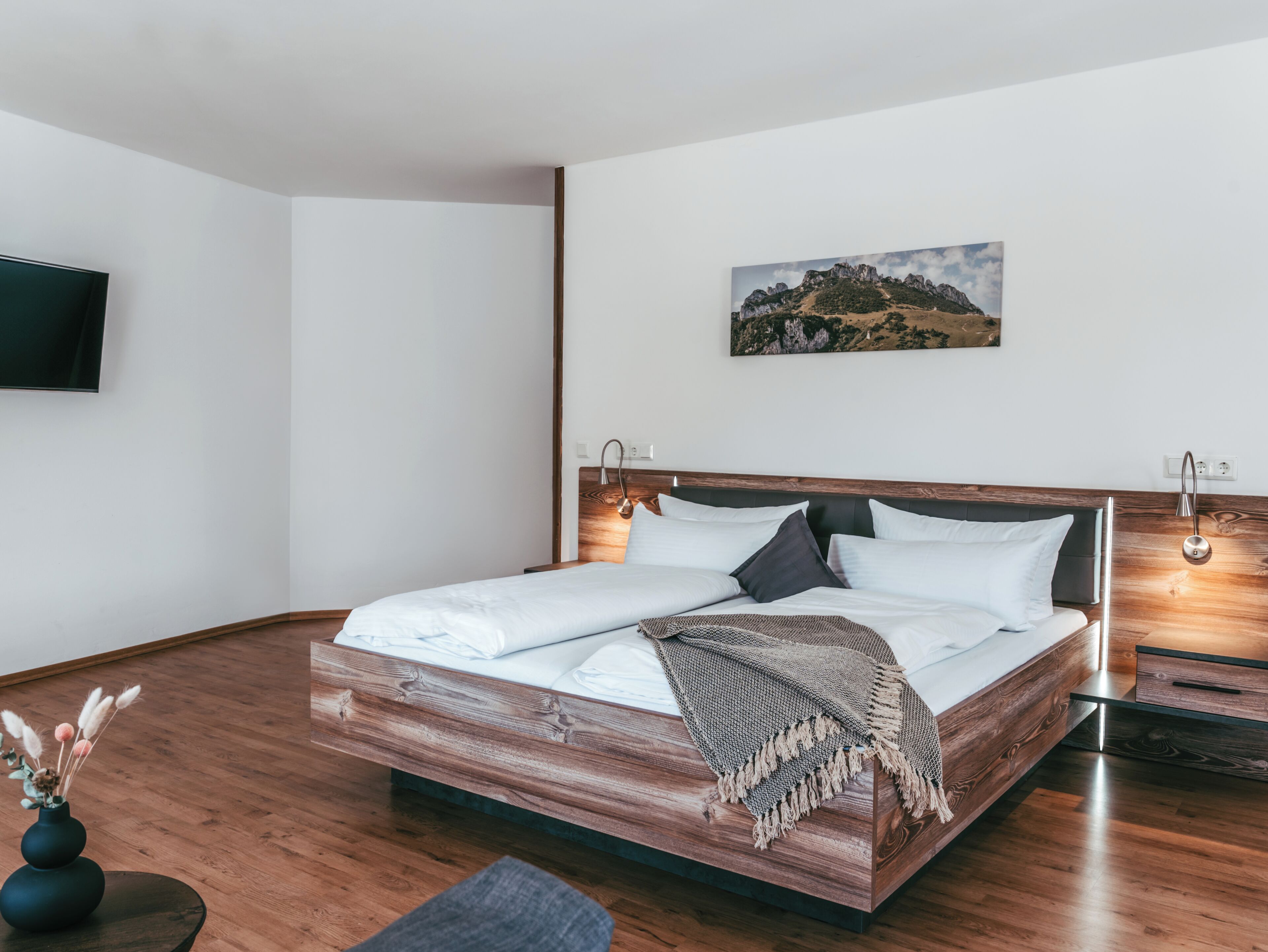 A modern bedroom with a wooden bed, a mounted TV, and a painting on the wall.