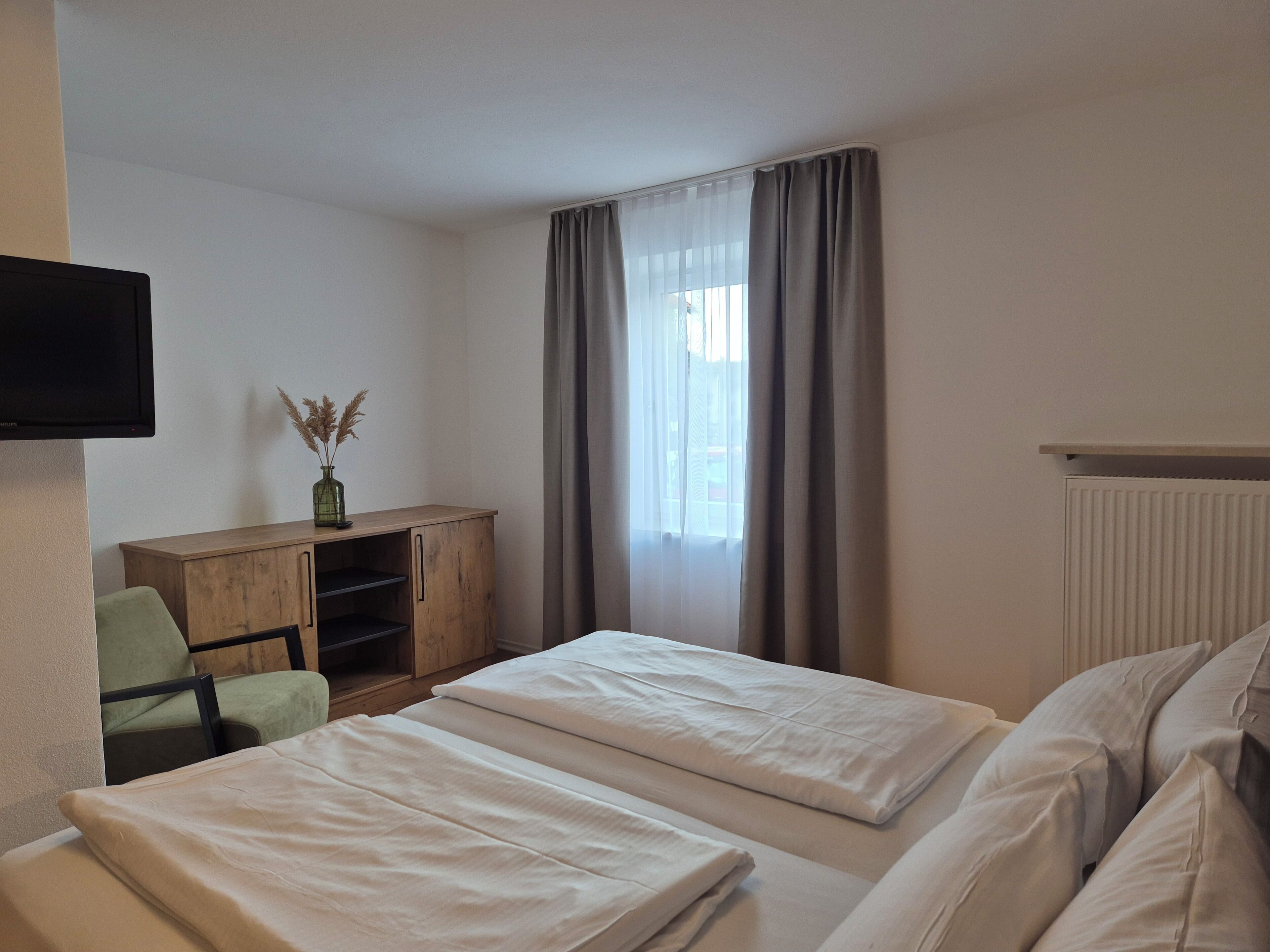 A hotel room with two beds, a desk, a chair, a television, and a window with curtains.