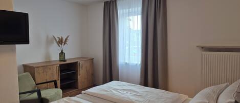 A hotel room with two beds, a desk, a chair, a television, and a window with curtains.