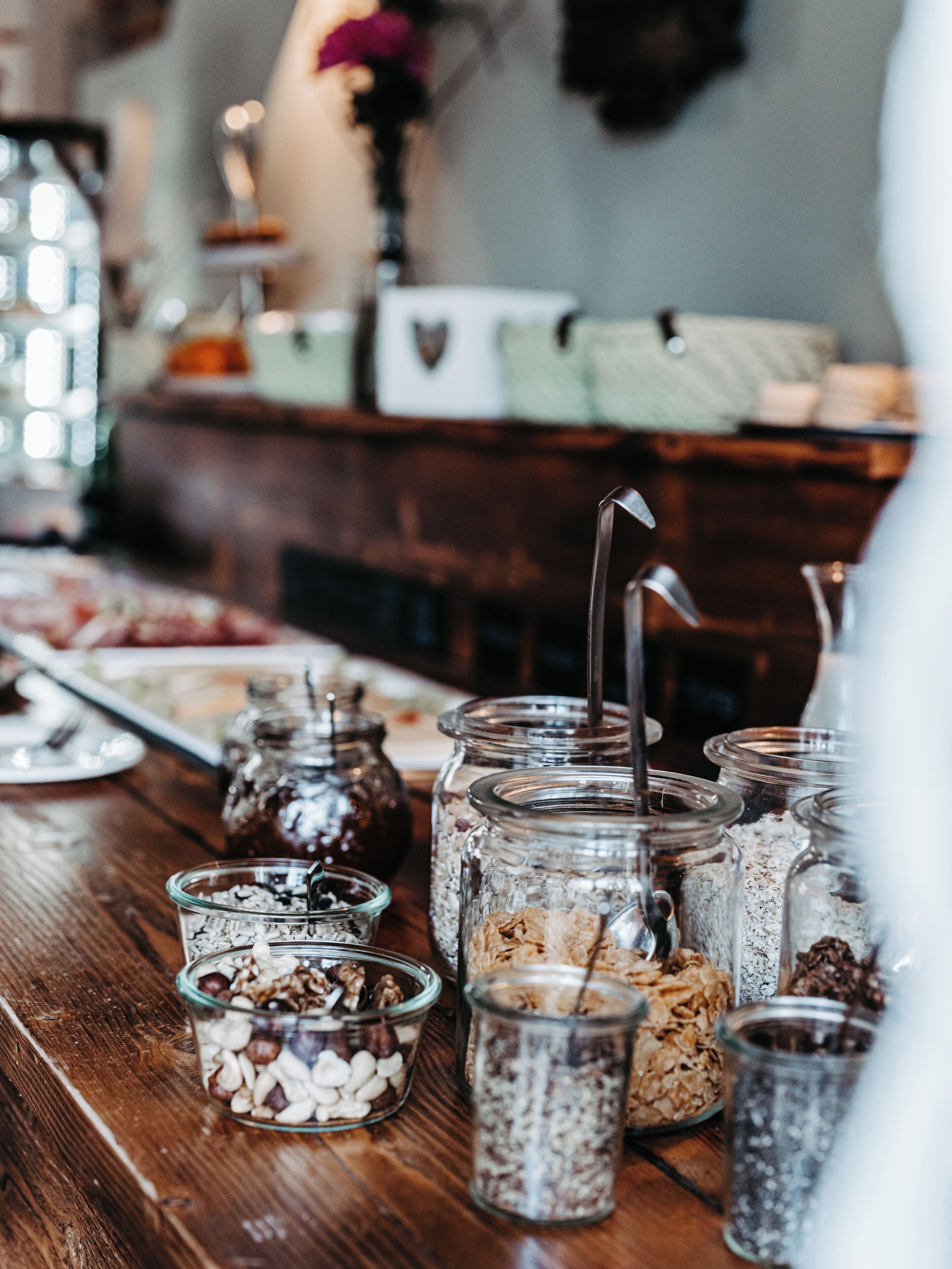 Una mesa de madera con diversos alimentos y recipientes, incluyendo frascos y cuencos con nueces y cereales.