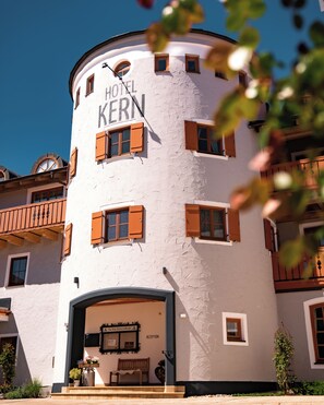 A hotel named 'HOTEL KERN' with a circular facade, multiple windows with shutters, and a reception area with a bench and potted plants. - Hotel Gasthof Kern (Halfing)
