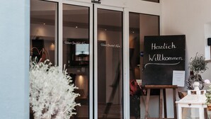 Entrada de hotel con techo de madera, puertas de cristal y un cartel de bienvenida.