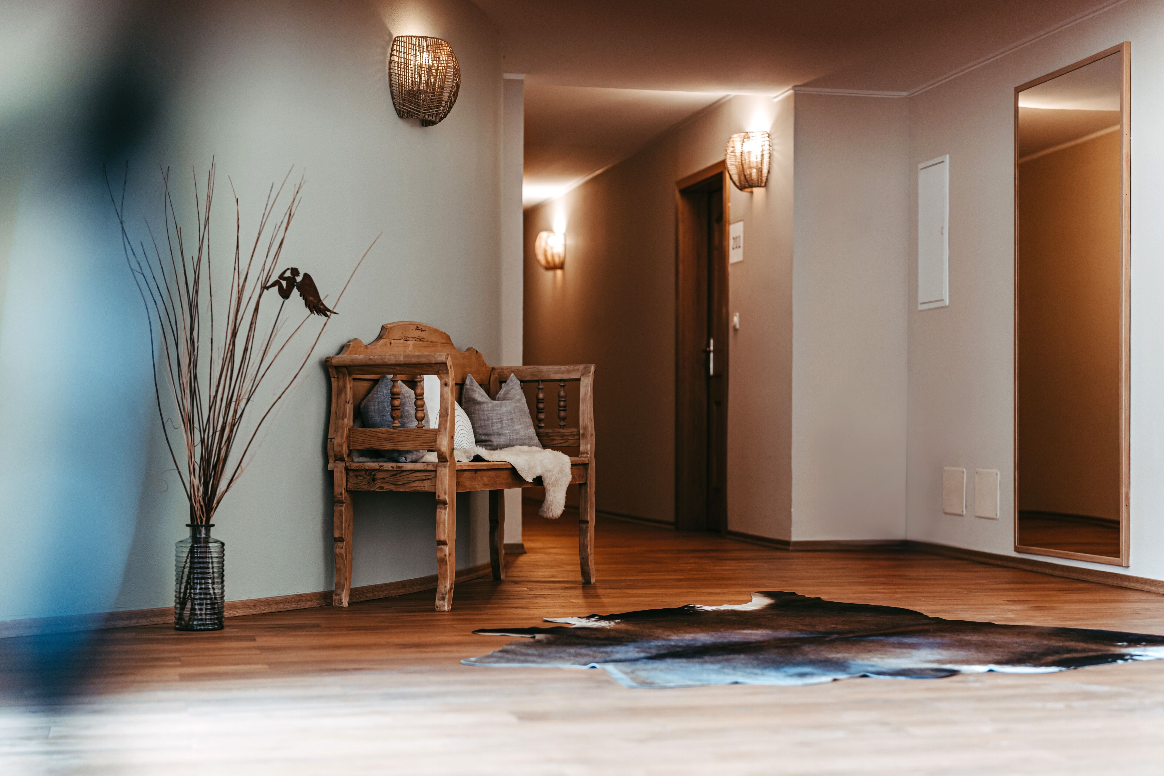 A hallway with a wooden bench, a vase with branches, and a cowhide rug.