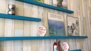 Een muur met houten latten en blauwe planken waarop verschillende items staan, waaronder een Wi-Fi wachtwoordbordje, een fles saus en een ingelijste foto.