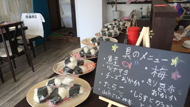 Een restaurantinterieur met een krijtbordmenu, borden met sushi en houten meubels.