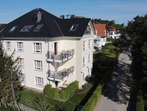 A multi-story residential building with a sloped roof, balconies, and a well-maintained lawn.