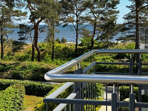 A metal railing overlooking a landscaped area with trees and a view of the sea. - Type I / Nr. 10 pages Sea view - beach house Aurell - directly on the Baltic Sea beach (Heringsdorf)
