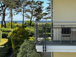 A balcony with a metal railing overlooking a landscaped garden and a body of water.