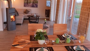 A dining area with a table set for two, a wood-burning stove, a sofa, and a painting on the wall.