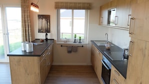 A compact kitchen with wooden cabinets, a black countertop, a window with a view, and a hanging towel rack.