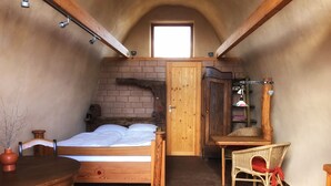 A cozy bedroom with a wooden bed, a small table, a chair, and a brick wall.