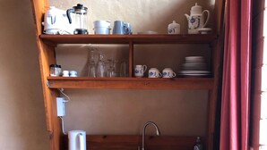 A compact kitchen with a wooden countertop, a sink, and a small refrigerator. There are shelves above holding various kitchenware and a kettle.