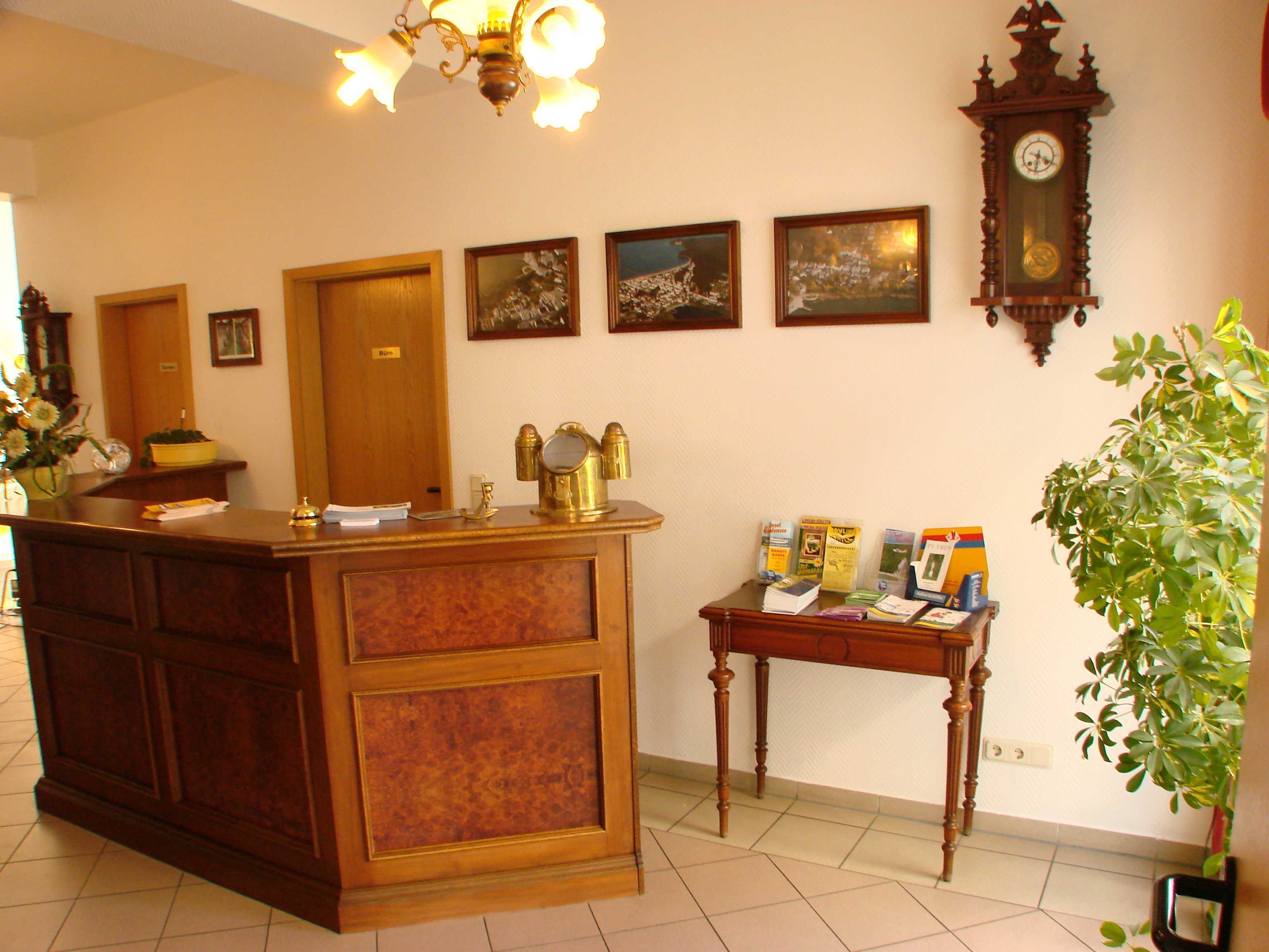 A reception desk with a wooden finish, a clock, framed pictures on the wall, and a small table with brochures.