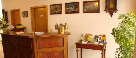 A reception desk with a wooden finish, a clock, framed pictures on the wall, and a small table with brochures.