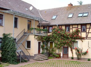 Un edificio de dos pisos con un balcón, una escalera y un jardín.