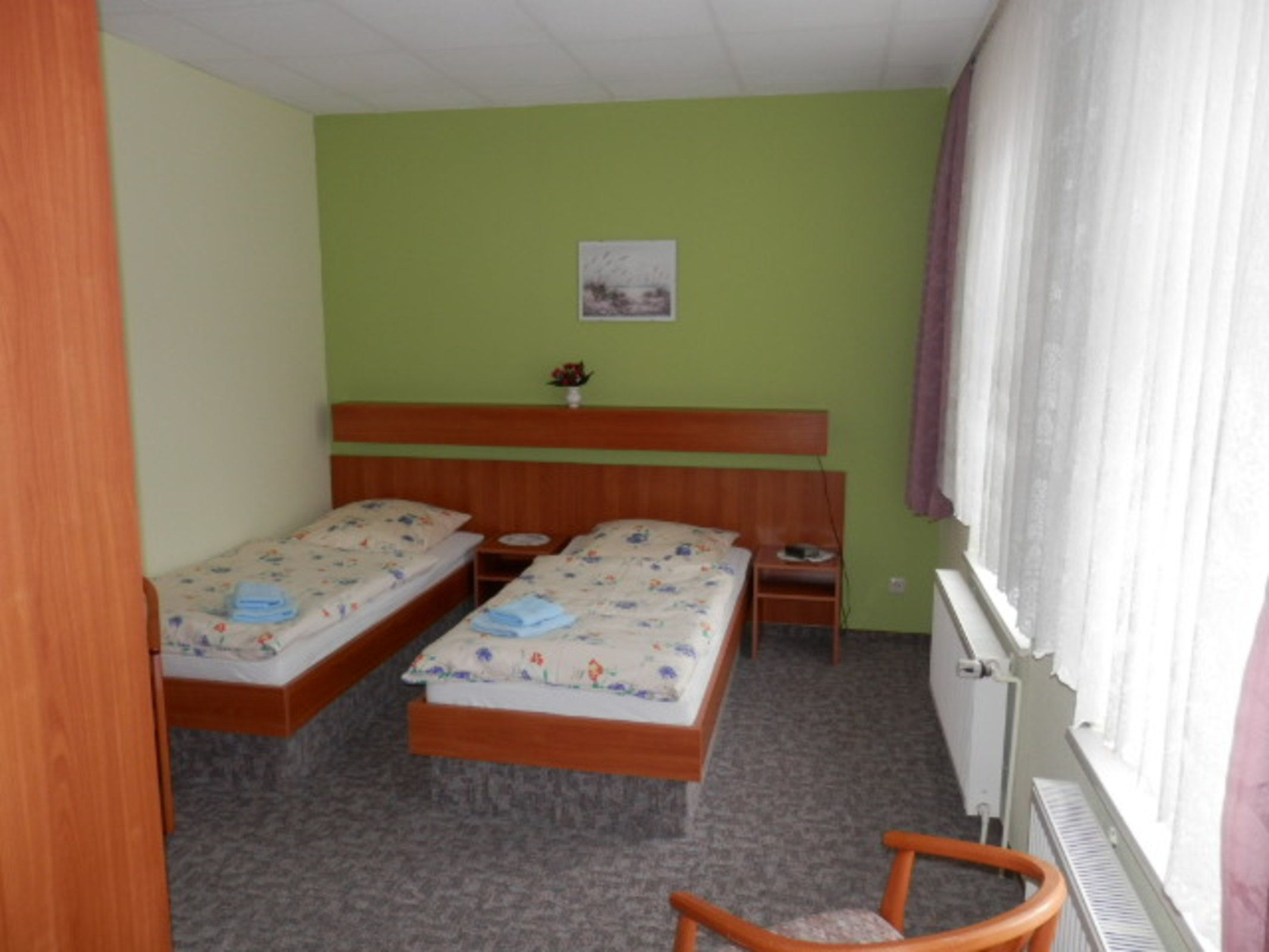 Una habitación con dos camas individuales, un cabecero de madera, una mesita pequeña, una silla y un radiador.