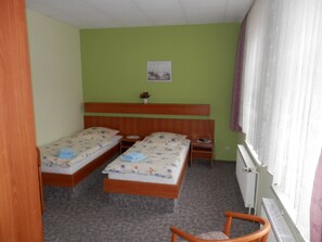 Una habitación con dos camas individuales, un cabecero de madera, una mesita pequeña, una silla y un radiador.