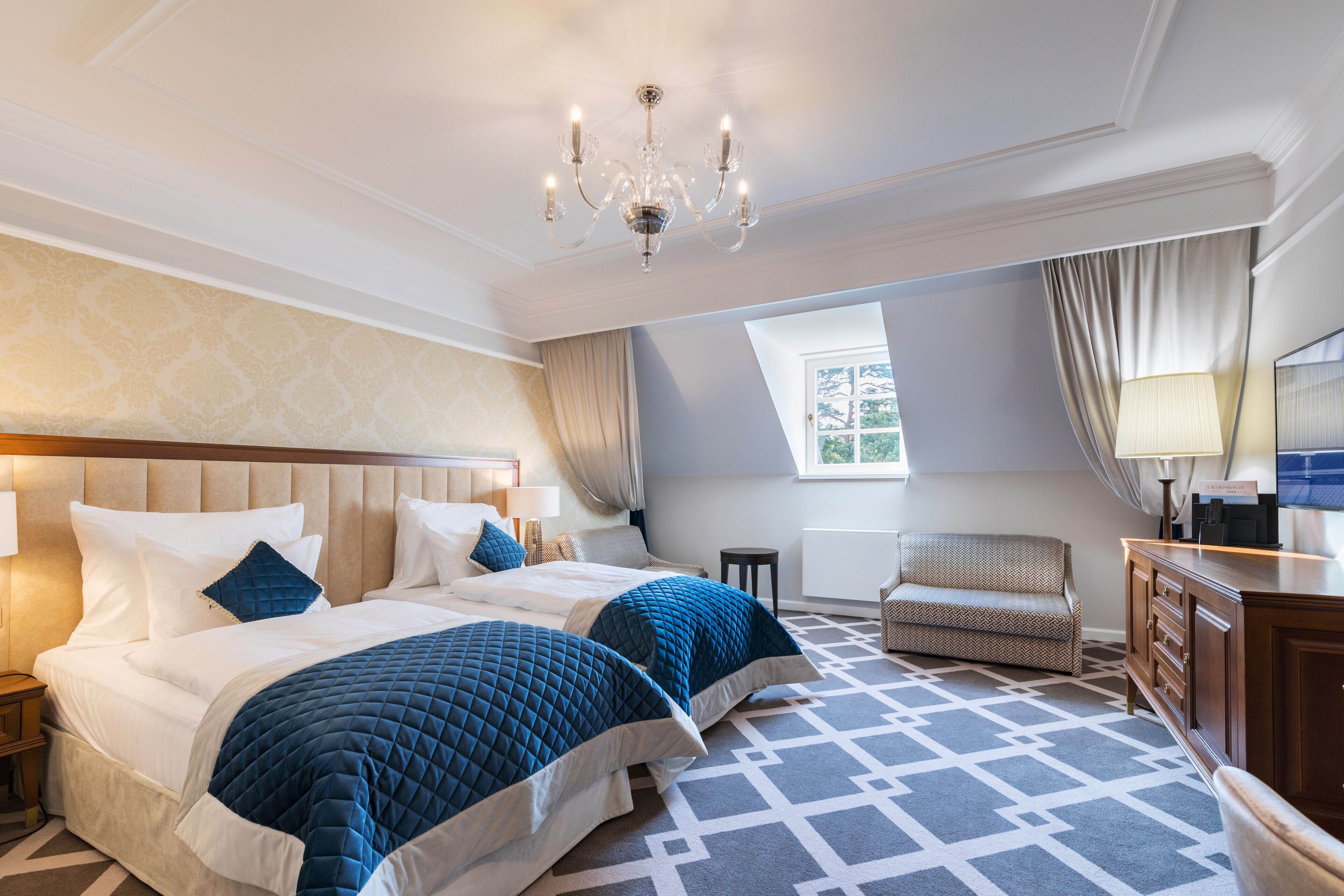 A hotel room with two beds, a chandelier, a sofa, and a desk.