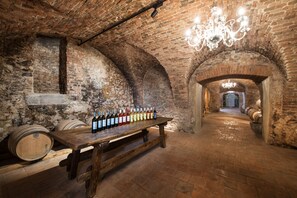 A wine cellar with wooden barrels and a long table displaying wine bottles. - Palace Art Hotel Pezinok (Pezinok)