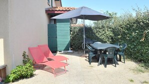 An outdoor patio with a table and chairs, a red lounge chair, and a green shed.