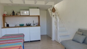 A compact living space with a kitchenette, a sofa, a dining table, and a staircase.