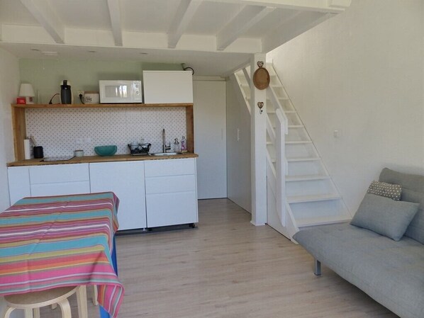 Un espace de vie compact comprenant un coin cuisine, un canapé, une table à manger et un escalier.