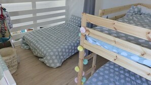 A room with two bunk beds, a window with white blinds, and a small table with a basket.
