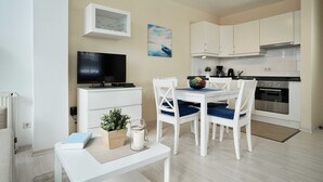 A modern kitchen with white cabinets, a built-in oven, and a dining area with a white table and chairs. - 08 Ferienappartement Mönchgut (H) - Apartment house Haus Arkona (Sellin)