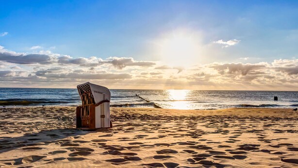 Una silla de playa y una estructura de madera en una playa arenosa, con el océano y una puesta de sol al fondo.